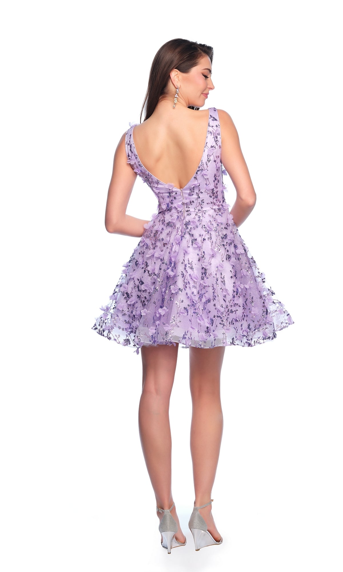 A woman models the Dave and Johnny Short Purple Hoco Dress 11765, featuring a sleeveless design, sequin floral details, and a deep V-back, as she stands facing away in silver heels against a white background.